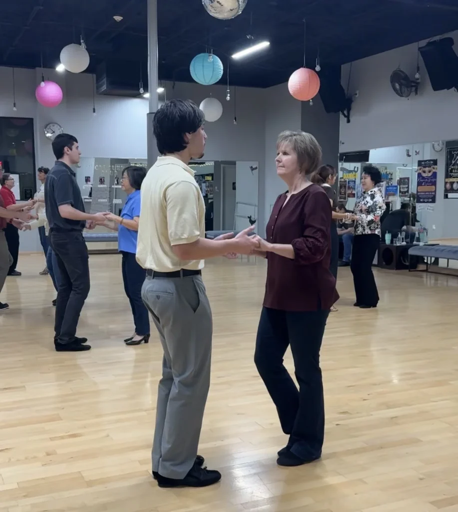 Two adults standing together during a beginner ballroom dance class in The Woodlands TX smiling and learning in a group setting