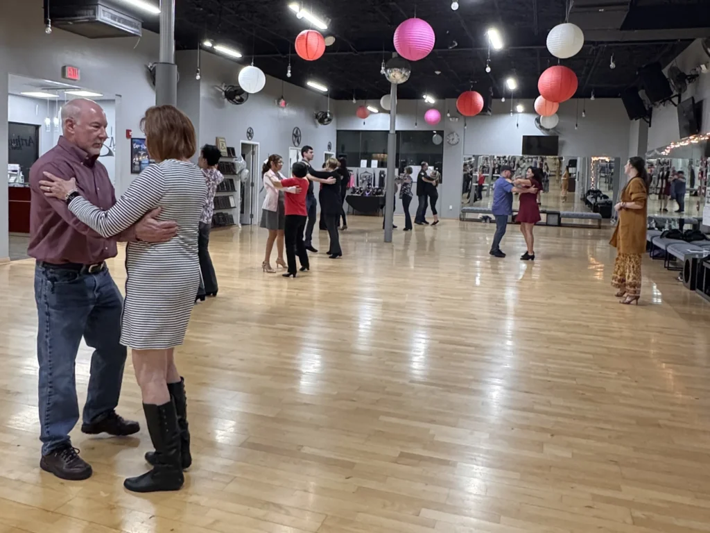 Beginner adult dance class with couples learning basic ballroom steps in a relaxed studio environment in The Woodlands TX